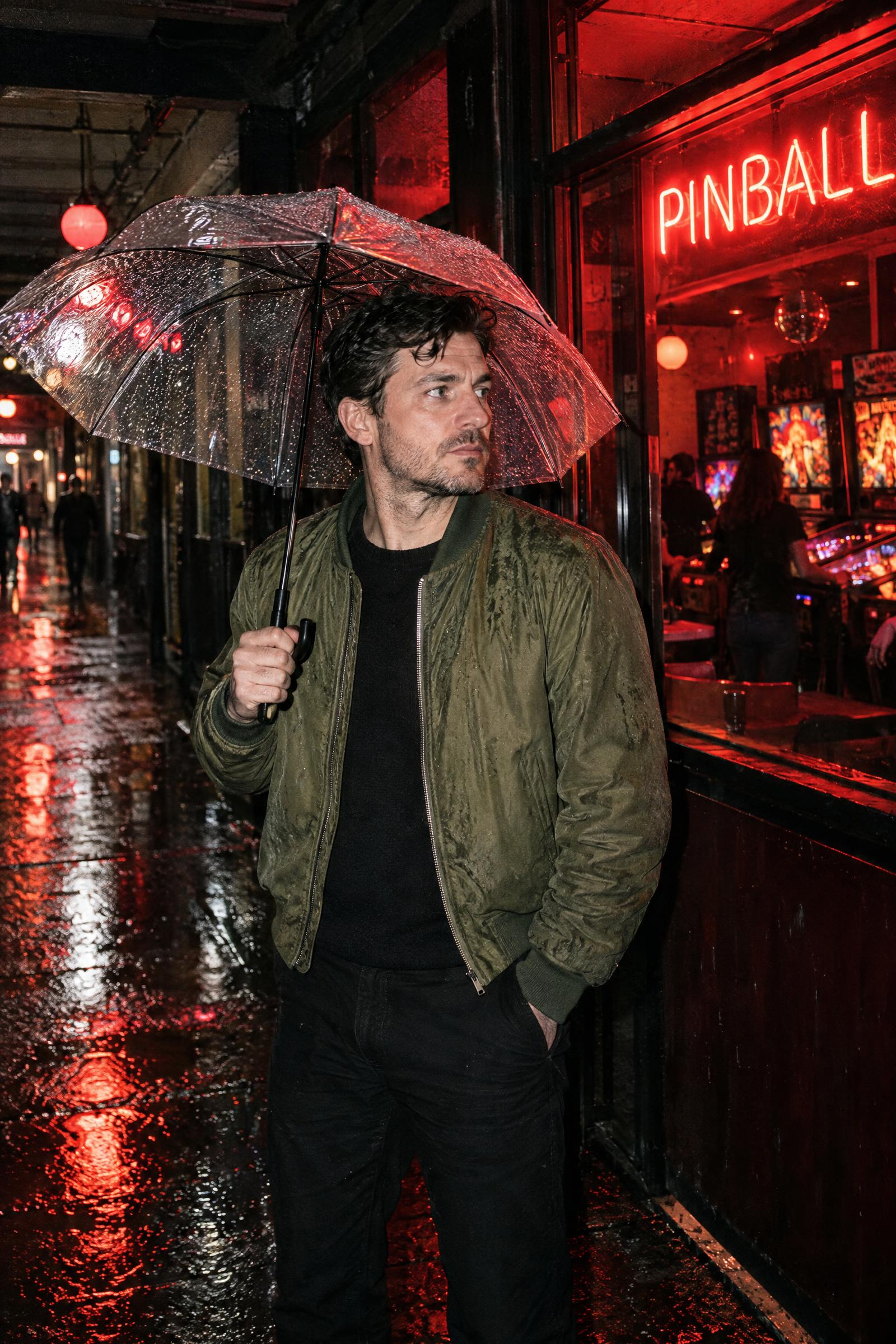 Man under an umbrella beside a neon pinball bar